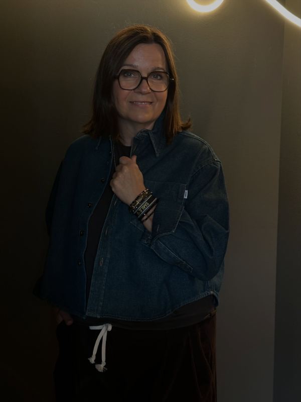 Ella in einer weiten Jeansjacke vor einer warm beleuchteten Wand